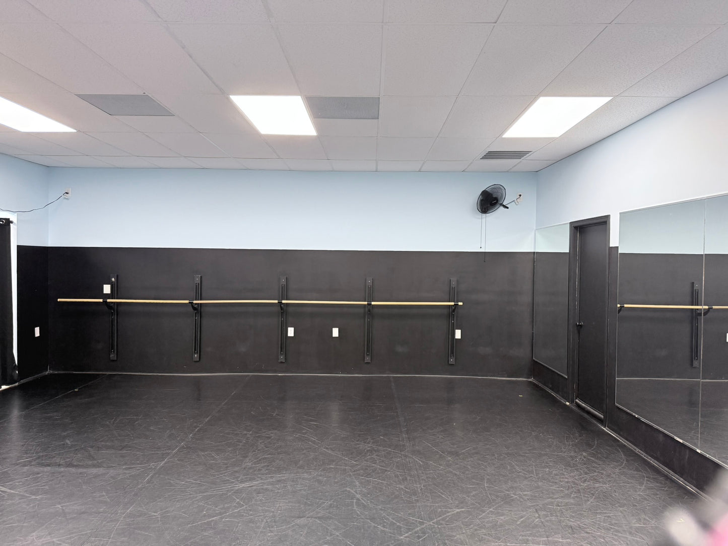 Dance studio with mirrors, barres, and a black floor.