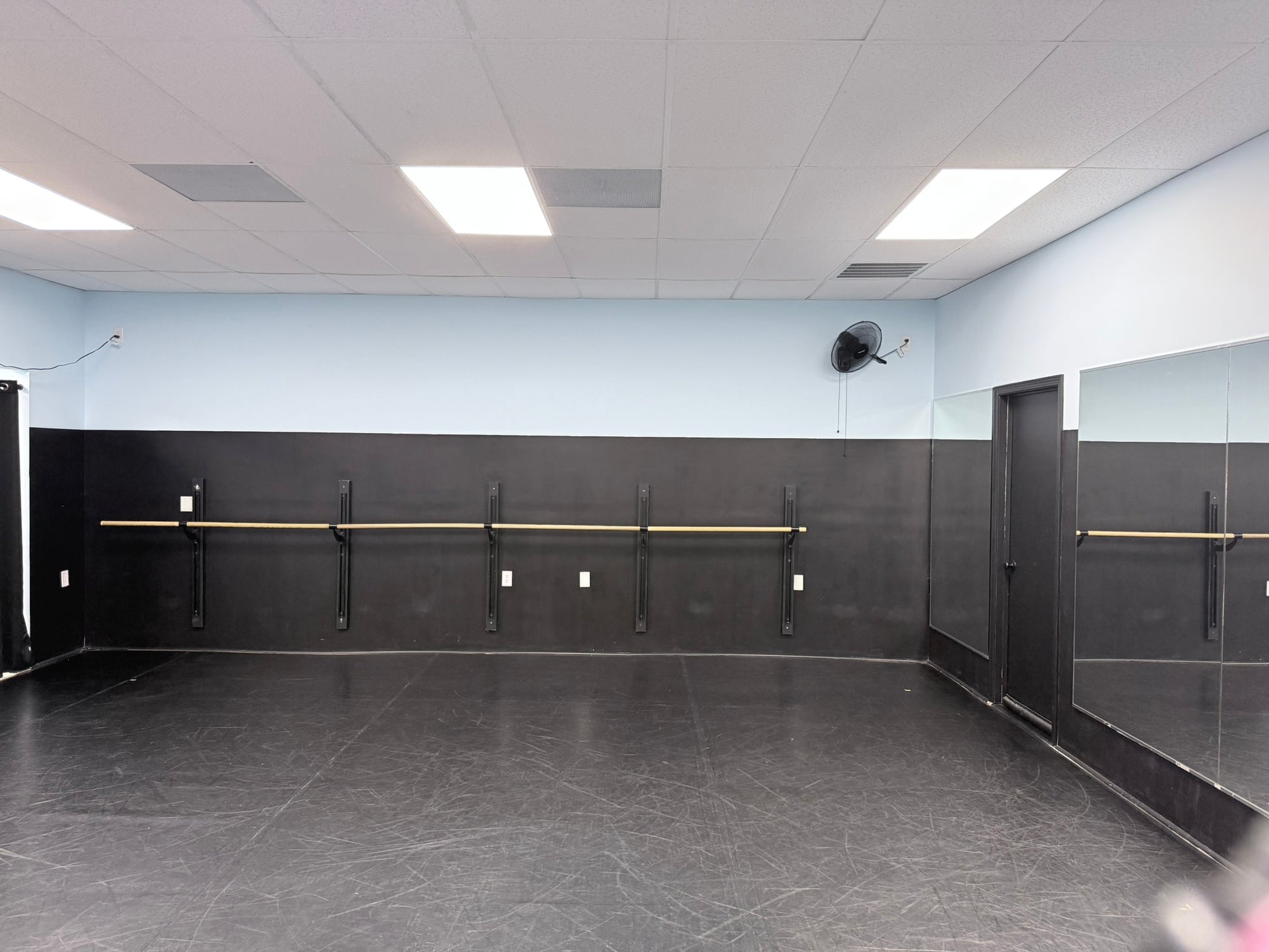 Dance studio with mirrors, barres, and a black floor.